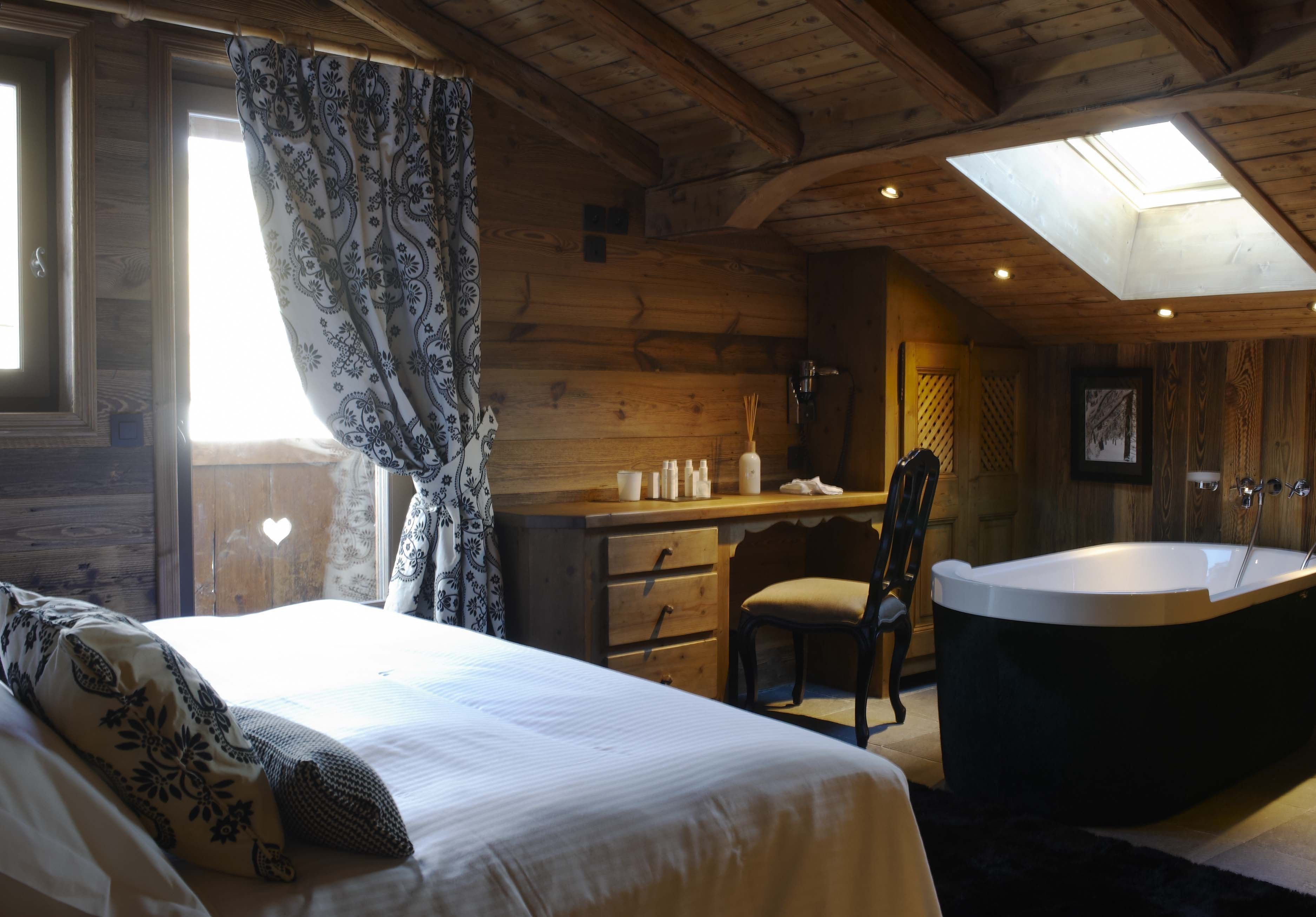 A wooden cabin bedroom with a bed, a desk, a chair, and a bathtub.