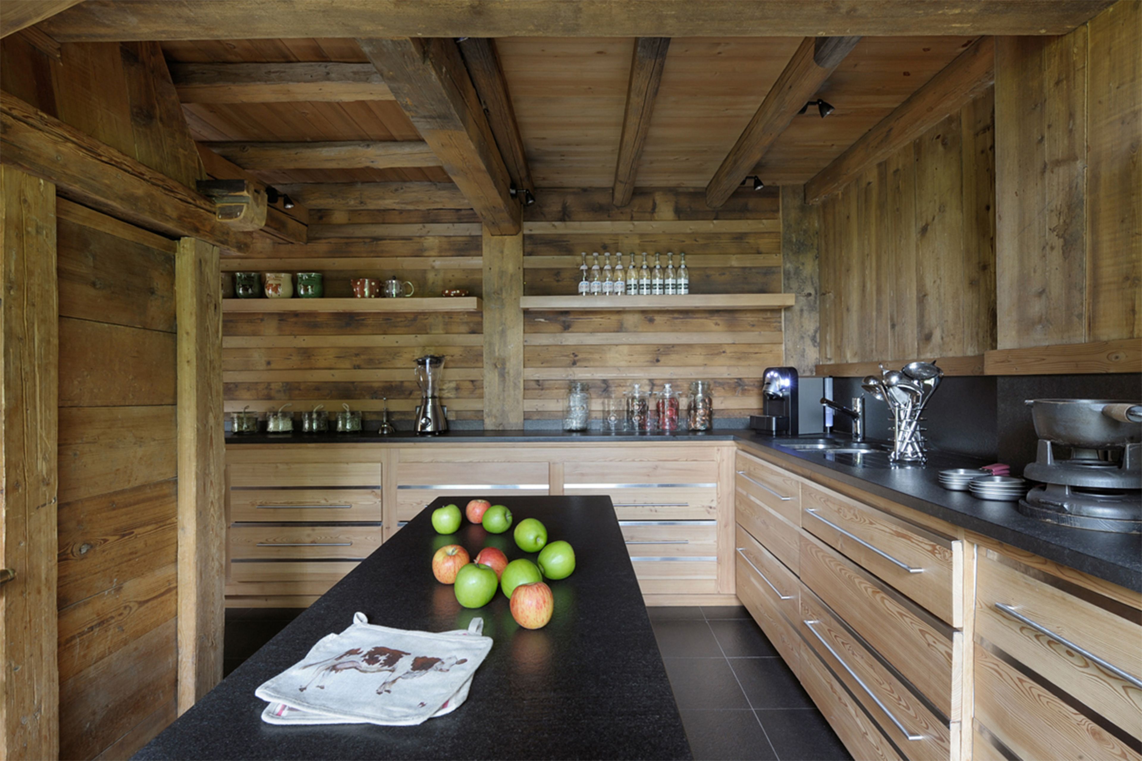 Une cuisine avec des meubles de rangement en bois, un plan de travail noir et un journal posé sur le plan de travail.