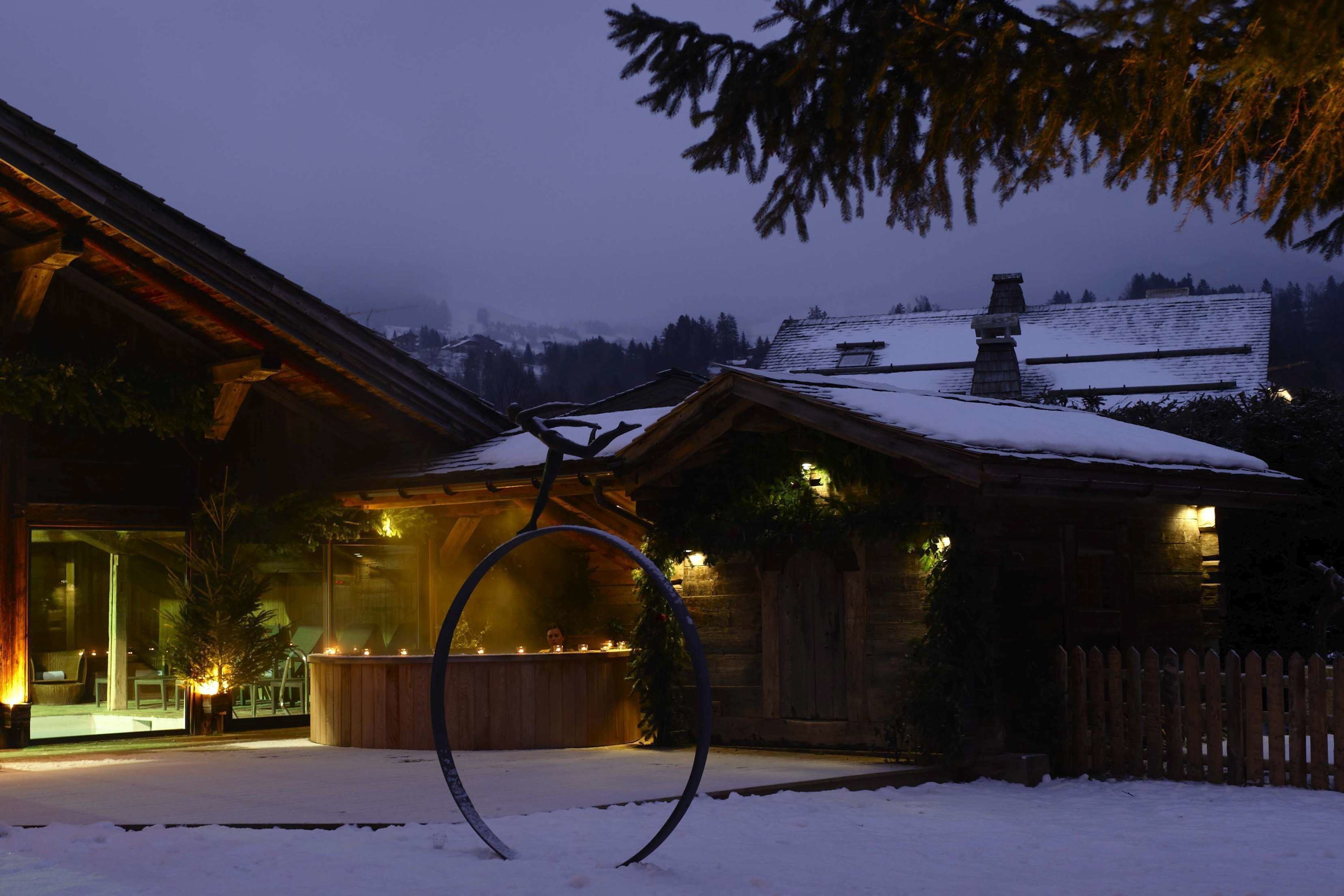 Una baita di legno con ingresso in vetro, un pontile di legno e un tetto imbiancato dalla neve.