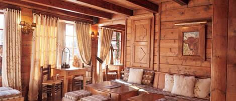 A cozy log cabin interior with a wooden dining table, benches, and cushioned seating.