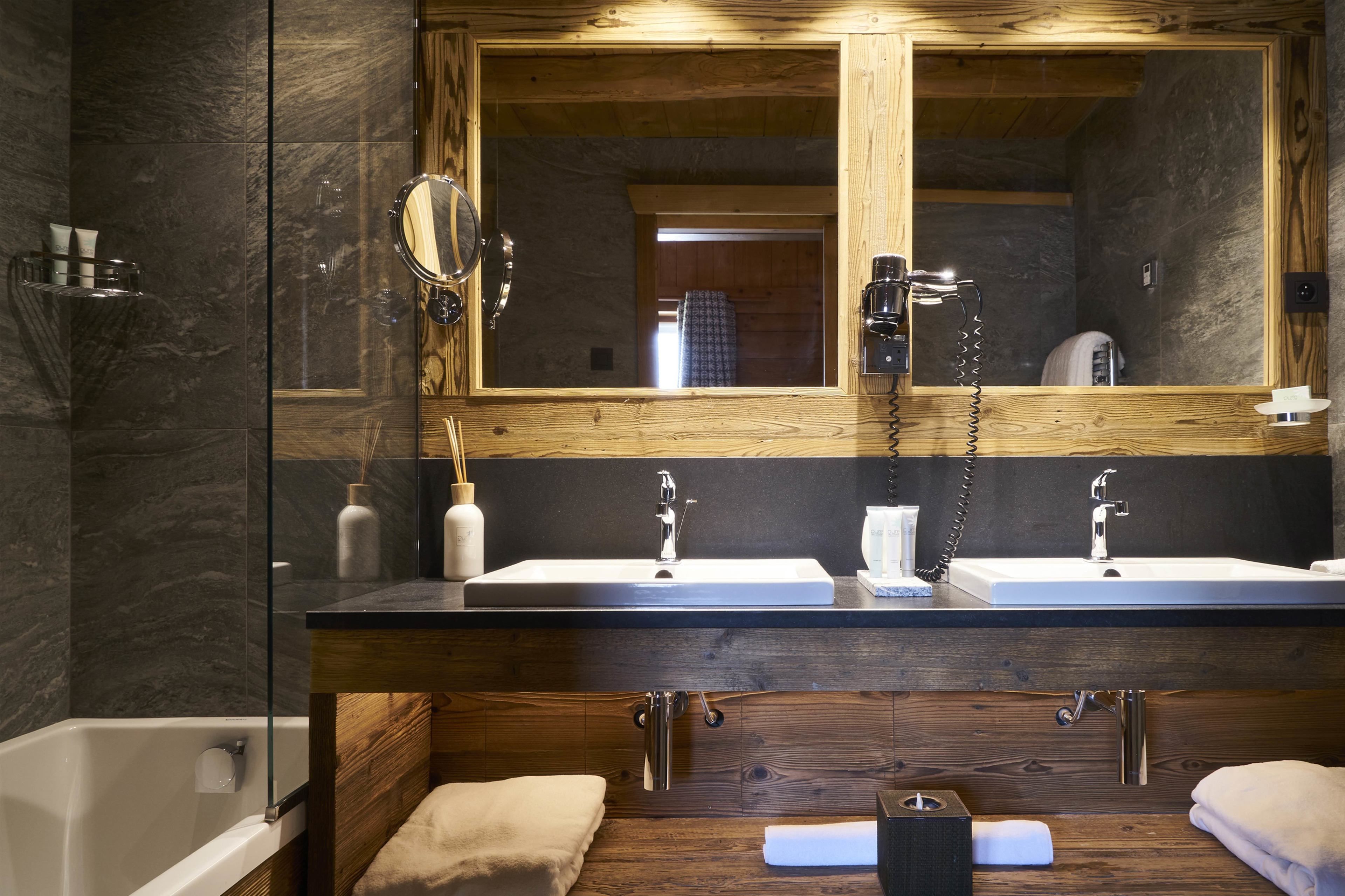 A modern bathroom with a wooden vanity, two sinks, a large mirror, and a glass shower enclosure.