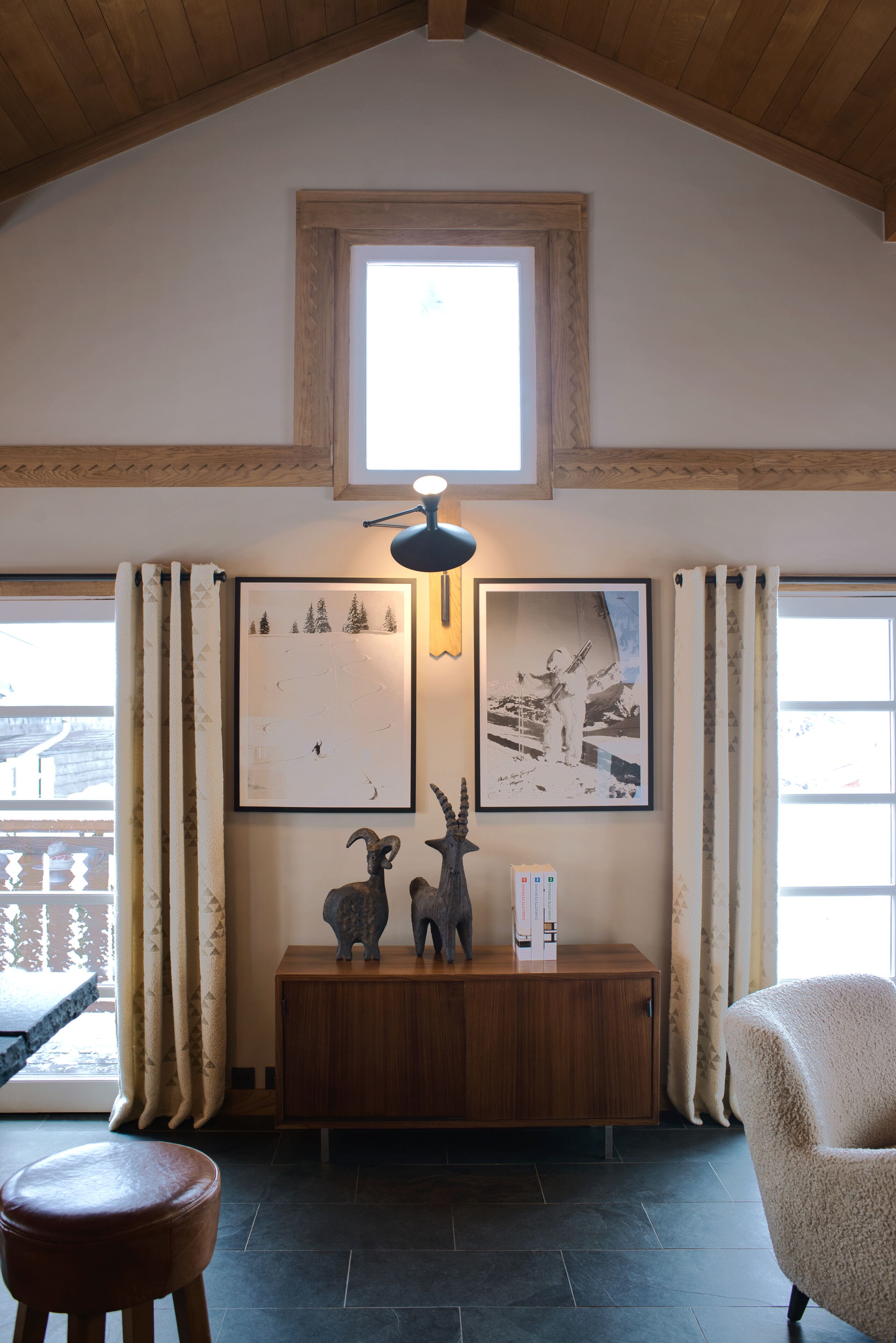 Una habitación con techo de madera, un ventanal pequeño, una consola de madera con dos esculturas, una silla y un cuadro grande en la pared.