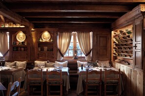 Cozy cabin dining area with a central table for two, wooden chairs, and a display of plates and bowls on shelves.