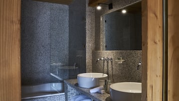 Une salle de bain moderne avec des murs en granit, deux lavabos, une baignoire et un grand miroir.