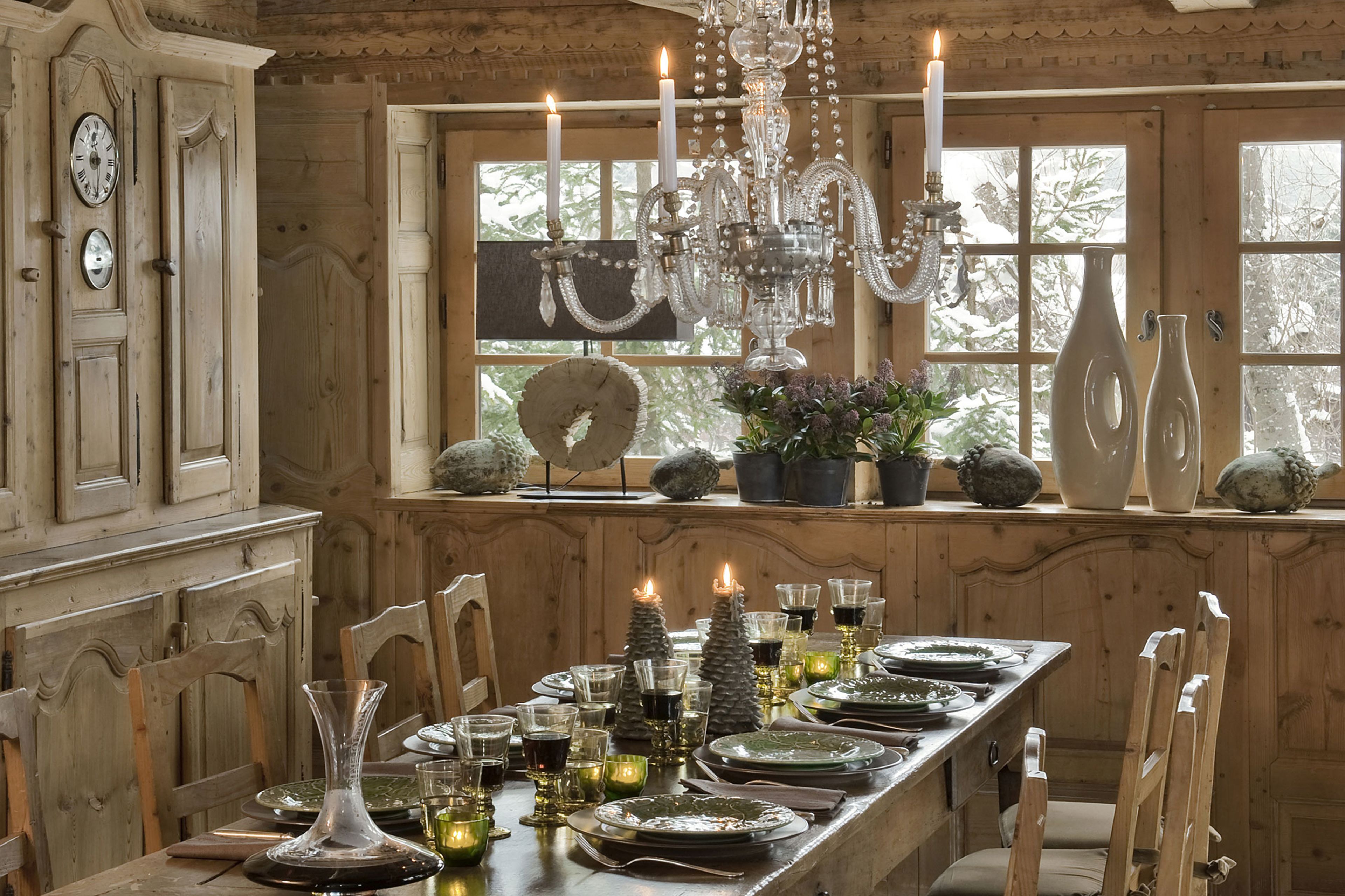 A wooden dining room with a long table set for six, candles, and a chandelier.