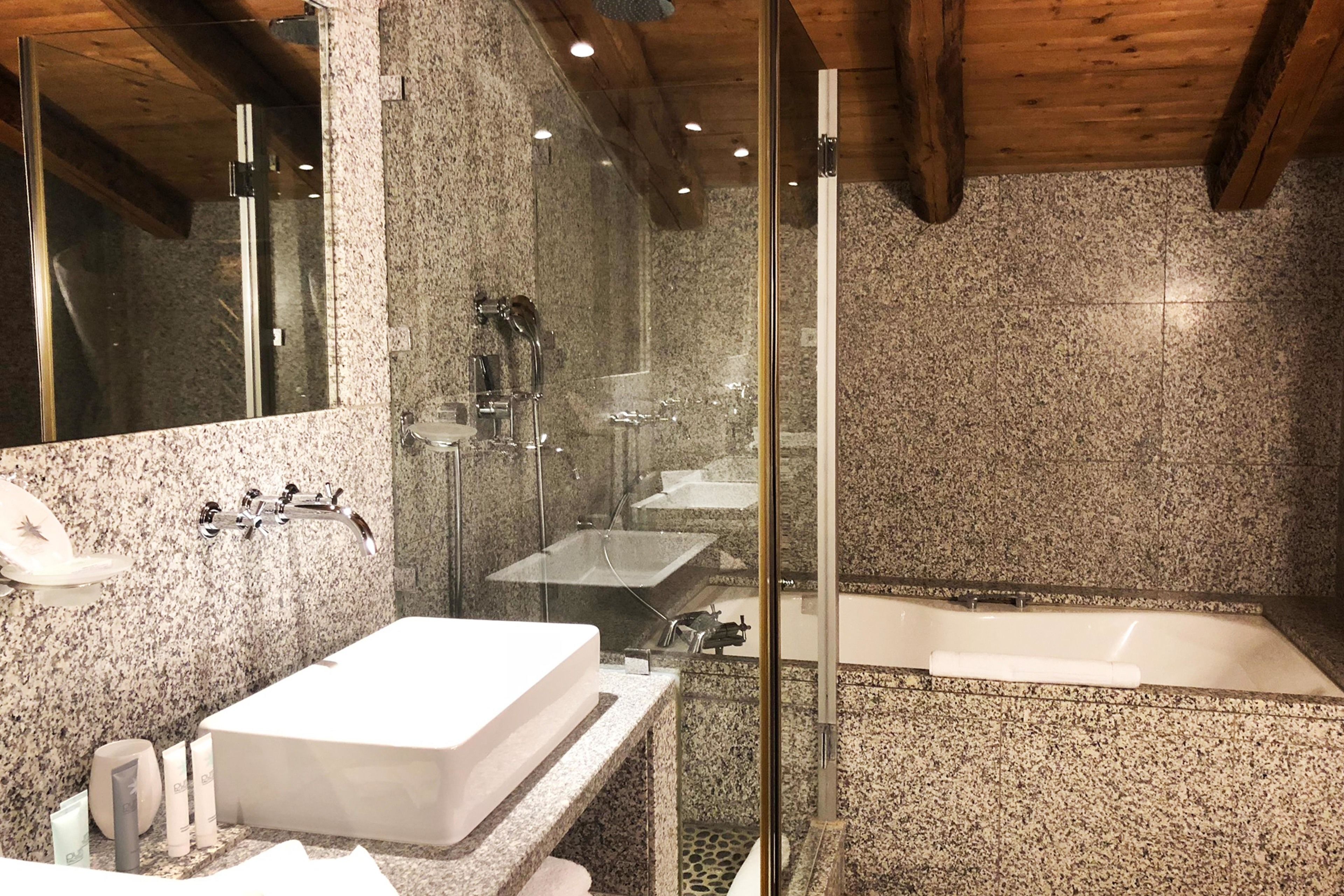 Een moderne badkamer met granieten aanrechtbladen, een groot wastafel, een bad en een douchecabine met glazen wanden.