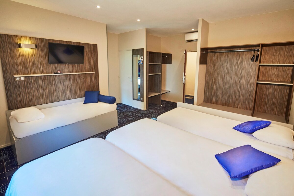 A hotel room with two beds, a TV mounted on the wall, a wardrobe, and a mirror.