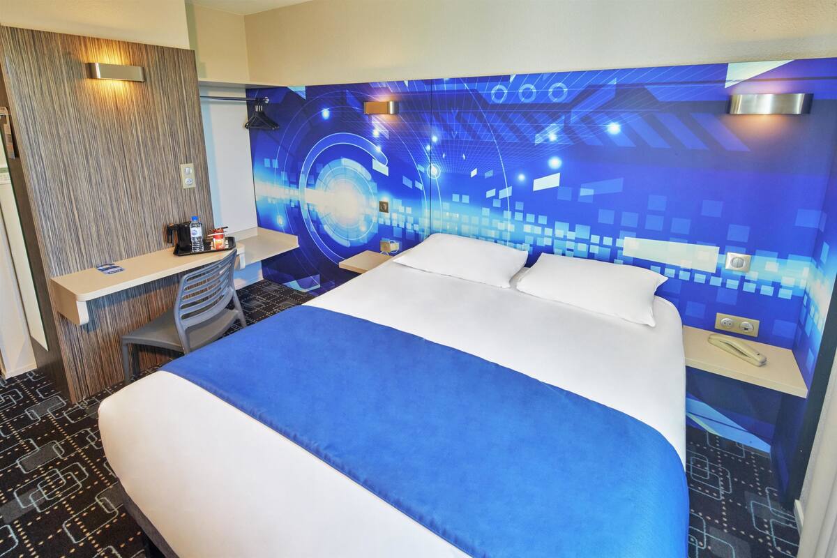 Ein Hotelzimmer mit einem großen Bett, einem Schreibtisch mit Stuhl und einer Wand mit einem blauen Design aus Schaltkreisen.