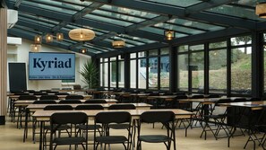 Une salle de conférence équipée de tables et de chaises, dotée de grandes fenêtres et d’une enseigne indiquant « Kyriad ».