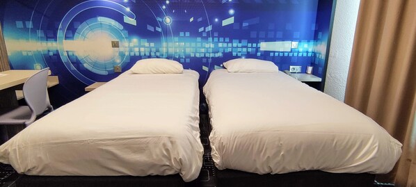 A hotel room with two single beds, a desk, and a chair.
