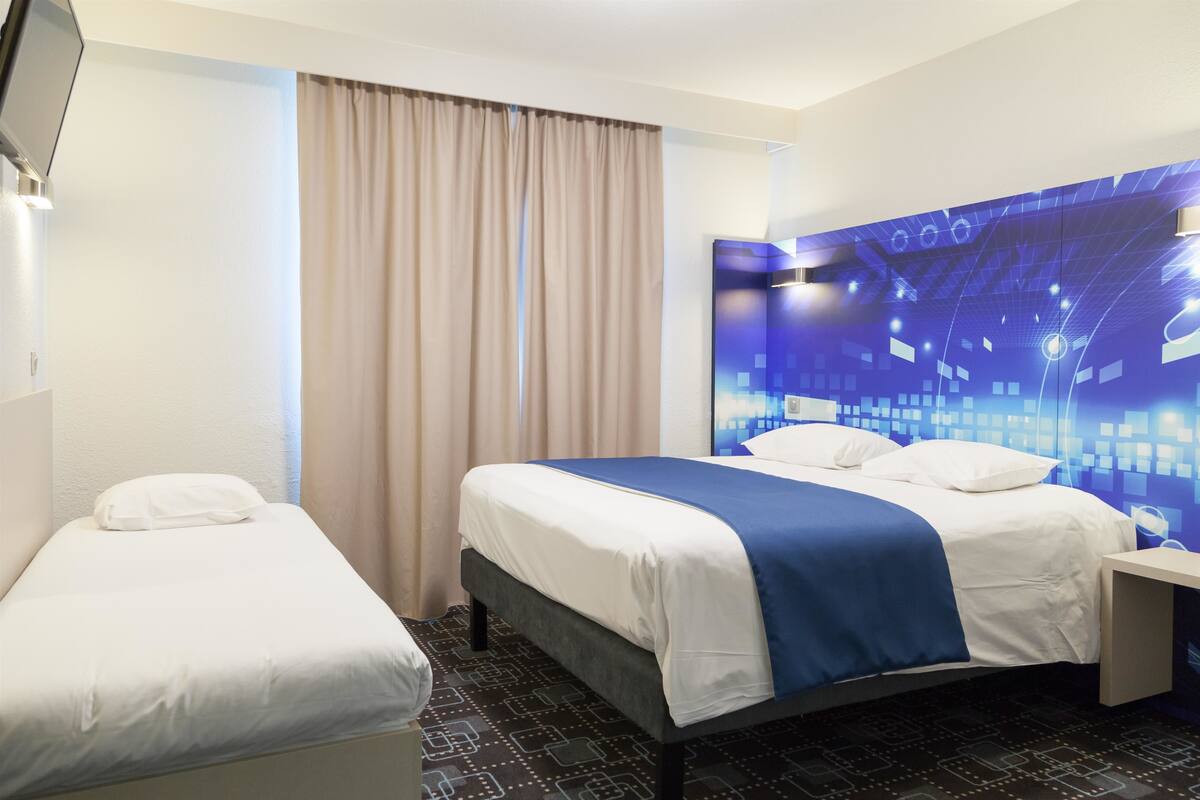 Ein Hotelzimmer mit Bett, Nachttisch, Vorhängen am Fenster und einer Wand mit geometrischem Muster.