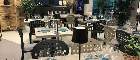 A restaurant interior with tables set for dining, a menu stand, and a bar area.