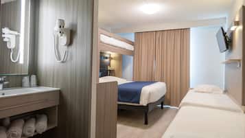 Una camera d'albergo con un letto a castello, un letto singolo, un bagno con lavabo e specchio, e una TV fissata al muro.