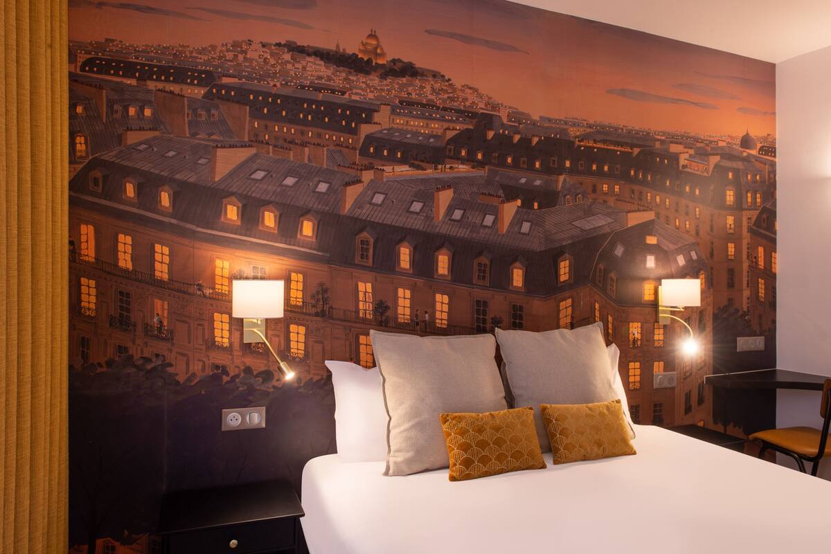A hotel room with a large bed, two bedside lamps, and a mural of a cityscape on the wall.