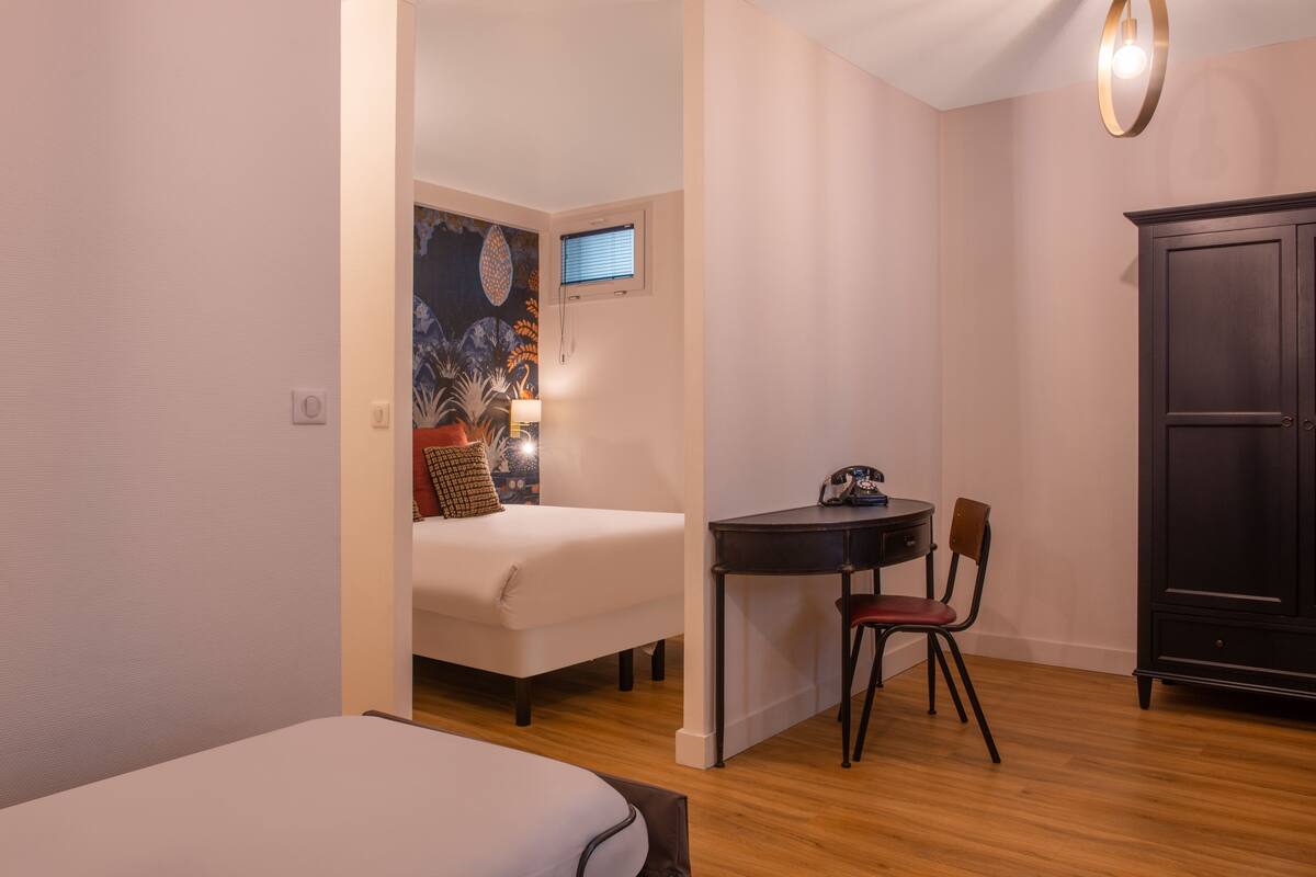 A compact room with a bed, a desk with a chair, a small table, and a cabinet.