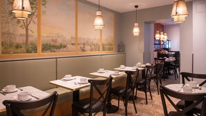 Un restaurant amb diverses taules i caires, un mural a la paret i làmpades penjants.