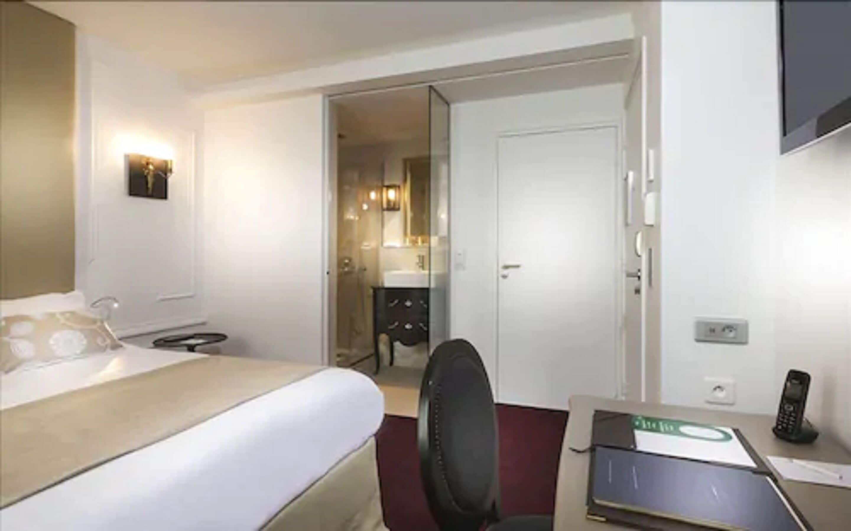 A hotel room with a bed, a desk with a telephone, and a mirror.