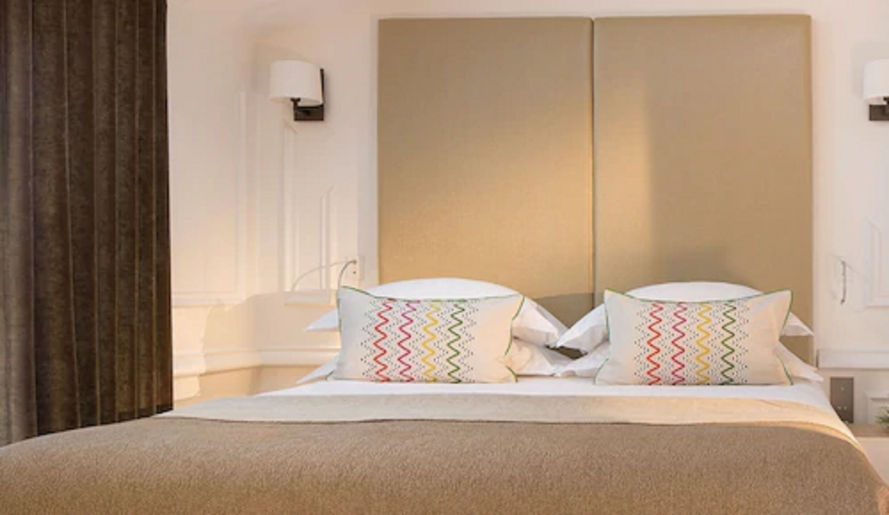 A bed with a beige bedspread and two pillows with a zigzag pattern.