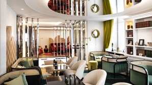 A modern interior with a circular ceiling design, a seating area with chairs and a table, and a bookshelf with books. - Hotel Victor Hugo Paris Kléber (Paris)