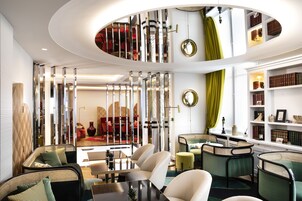 A modern interior with a circular ceiling design, a seating area with chairs and a table, and a bookshelf with books.