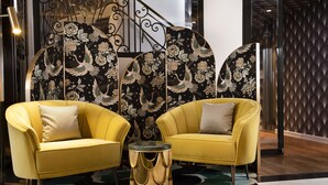 A modern lobby with two yellow armchairs, a round table, and decorative panels with floral and bird designs. - Hotel Victor Hugo Paris Kléber (Paris)