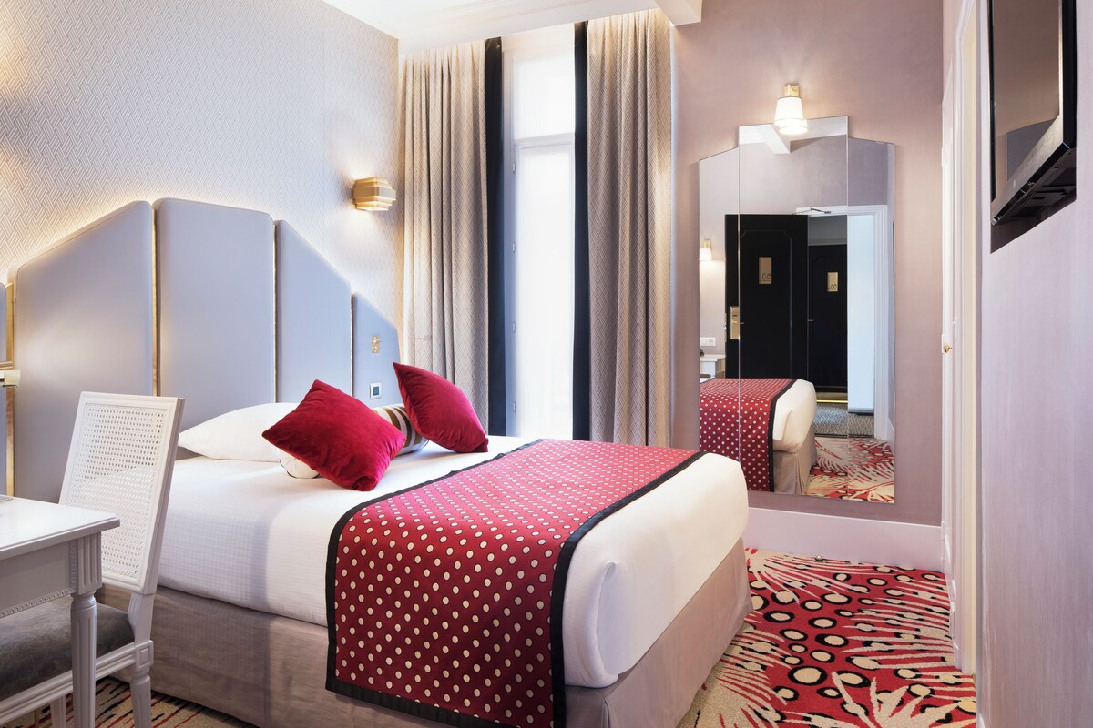A hotel room with a bed, a chair, a desk, and a mirror.