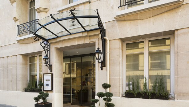 A building with a glass entrance, a metal balcony, and potted plants. - Hotel Victor Hugo Paris Kléber (Paris)
