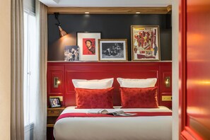 Un letto rifatto con cura, con biancheria rossa e bianca, un comodino con una lampada e una parete decorata con quadri.