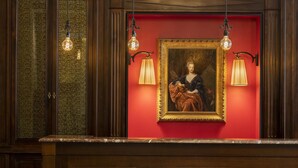 Un tableau encadré est accroché sur un mur rouge, et deux lampes sont fixées au mur de part et d’autre.