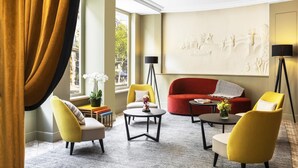 Un salon moderne avec un canapé rouge, des fauteuils jaunes et une petite table basse. On y trouve une bibliothèque, un lampadaire et un élément décoratif mural.