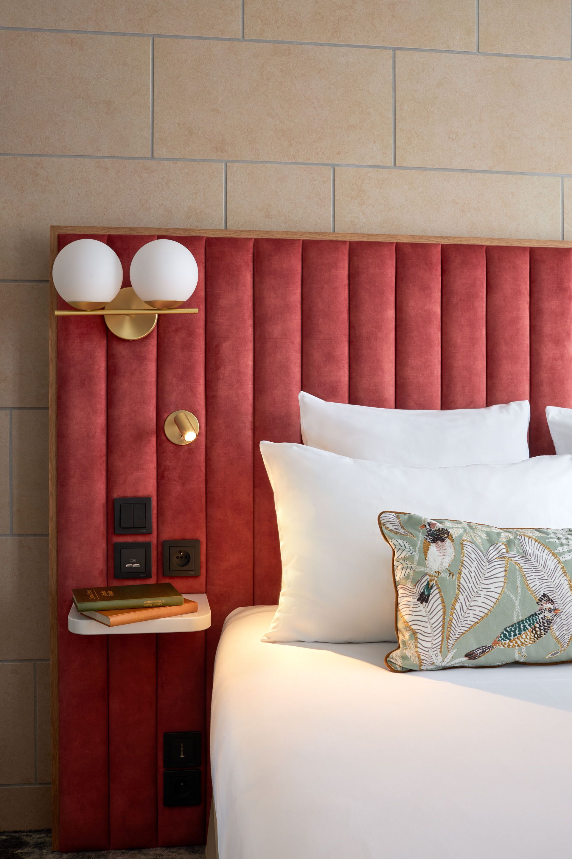 A hotel room with a red upholstered headboard, white bedding, and a decorative pillow.