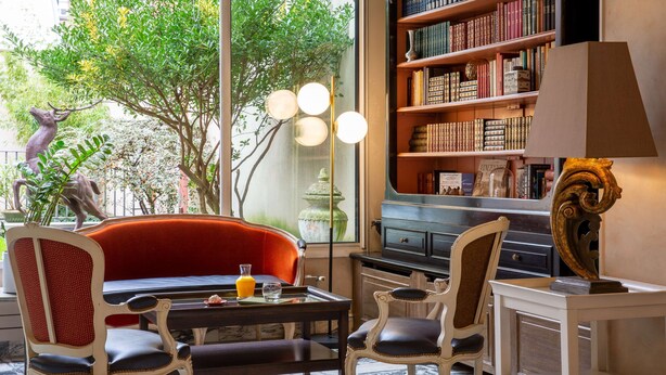 A room with a red sofa, two chairs, a table with a glass and a book, a bookshelf, and a lamp. - Best Western Saint Louis - Grand Paris Vincennes (Vincennes)
