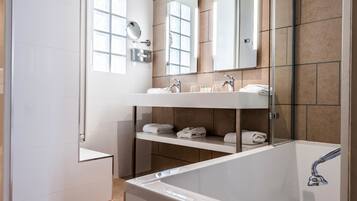 Ein modernes Badezimmer mit Badewanne, Waschbecken mit Spiegel und einem Regal mit Handtüchern.