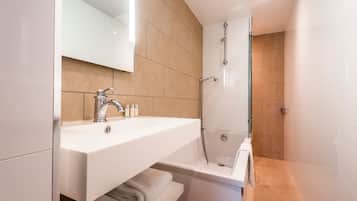 Een moderne badkamer met een witte wastafel, een douche met glazen wanden en beigetegels.