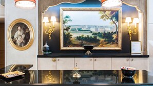 A reception area with a large framed painting, a round portrait, and a reception desk with a bowl and a menu. - Best Western Saint Louis - Grand Paris Vincennes (Vincennes)