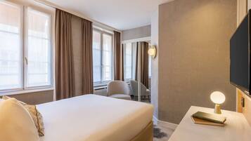 A hotel room with a bed, a desk with a lamp, a chair, and a TV mounted on the wall.