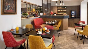 A dining area with a central island, red and yellow chairs, breakfast items, and a coffee machine. - Best Western Saint Louis - Grand Paris Vincennes (Vincennes)