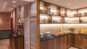 A breakfast bar with various food items and beverages, wooden paneling, and a brick wall. - Hôtel Brittany Opéra (Paris)