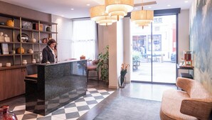 A hotel reception area with a marble counter, pendant lighting, a checkered floor, and a large window offering a view of the street. - Hôtel Brittany Opéra (Paris)