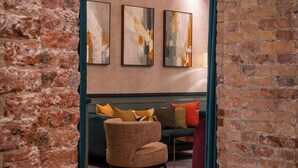 A room with a brick wall, wooden floor, and a seating area with a chair and cushions. - Hôtel Brittany Opéra (Paris)