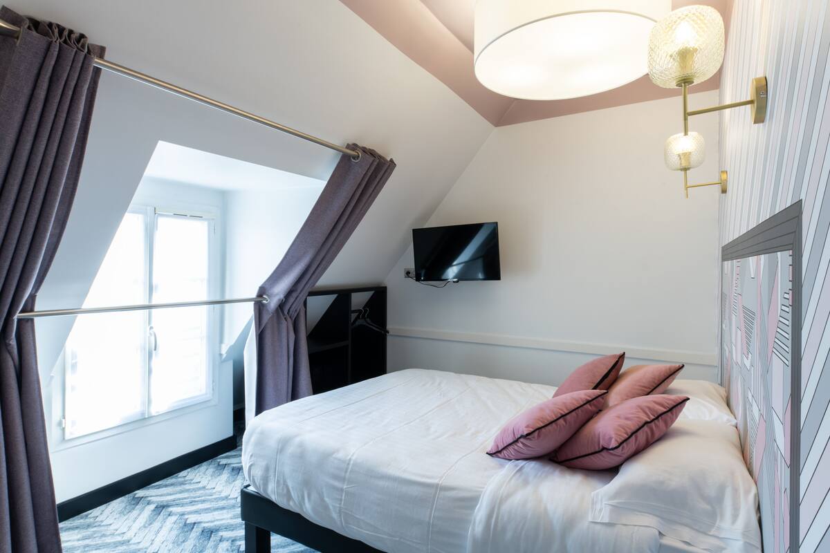 Un dormitorio con cama, televisor montado en la pared y ventana con cortinas.
