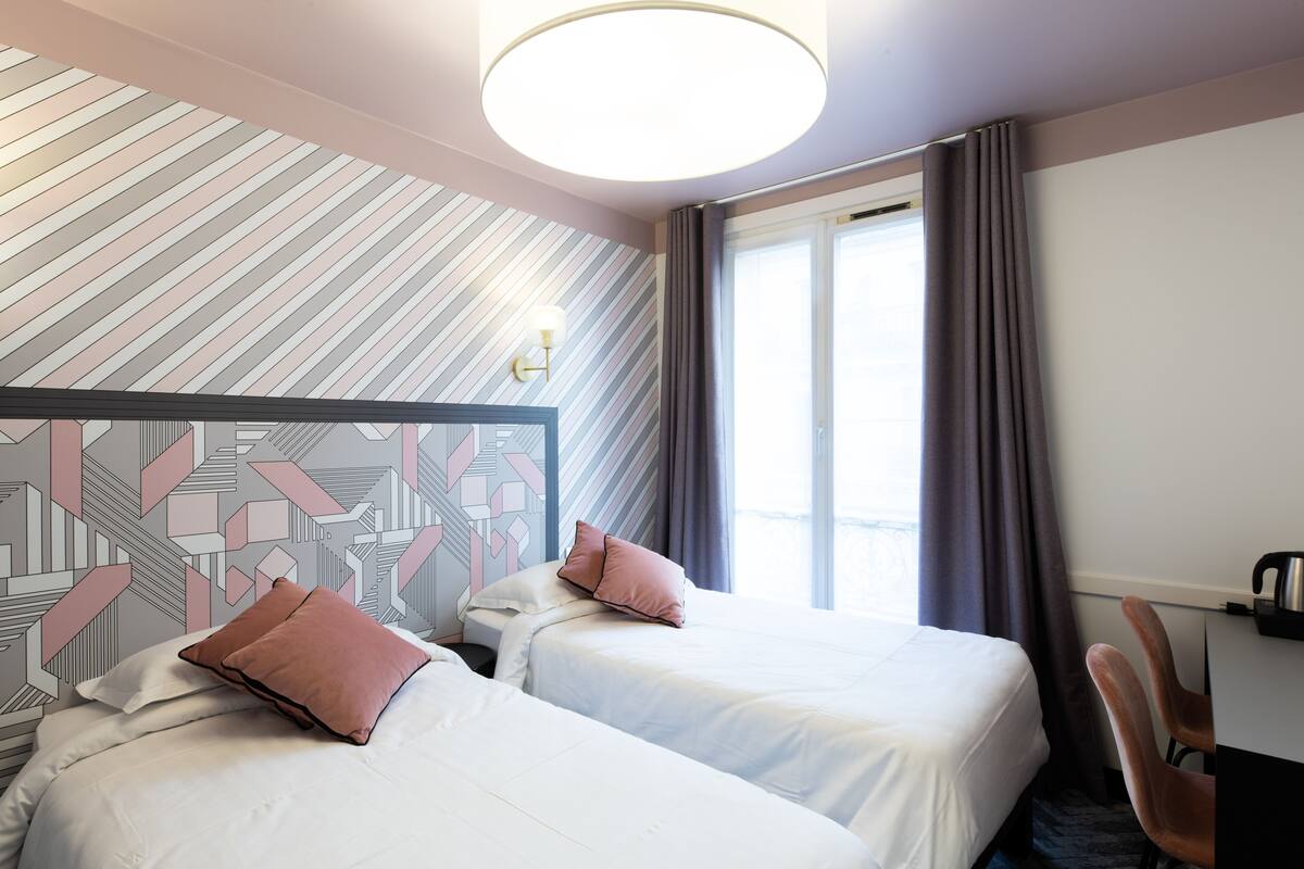 Una habitación de hotel con dos camas, un escritorio y un ventanal con cortinas.