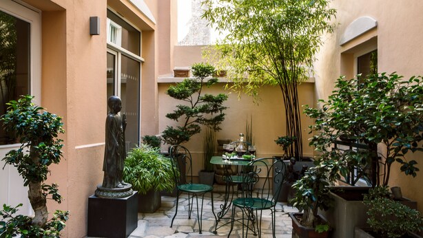 A courtyard with a statue, potted plants, and a table with chairs. - VLH Montparnasse Eiffel (Paris)