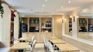 A modern restaurant with wooden tables and chairs, a kitchen area, and a seating area with a sofa. - VLH Montparnasse Eiffel (Paris)