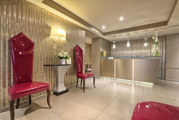 A hotel lobby with two red chairs, a reception desk, and a decorative wall with vertical lines. - Hôtel Mondial (Paris)