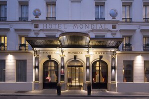 The exterior of Hotel Mondial with its classic architecture, large arched entrance, and illuminated signage. - Hôtel Mondial (Paris)