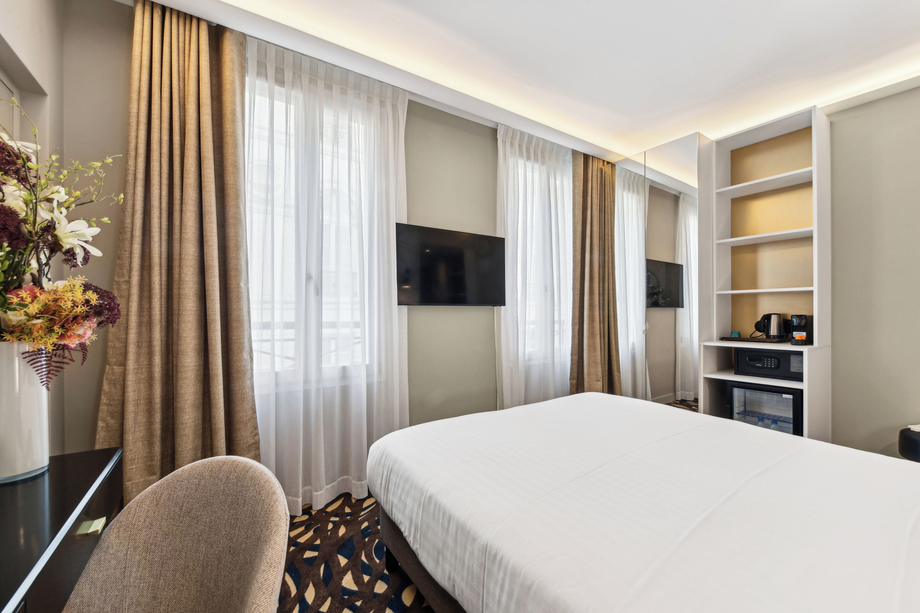 Une chambre d’hôtel dotée d’un grand lit, d’un téléviseur à écran plat fixé au mur, d’un bureau avec une chaise et d’un mini-bar.
