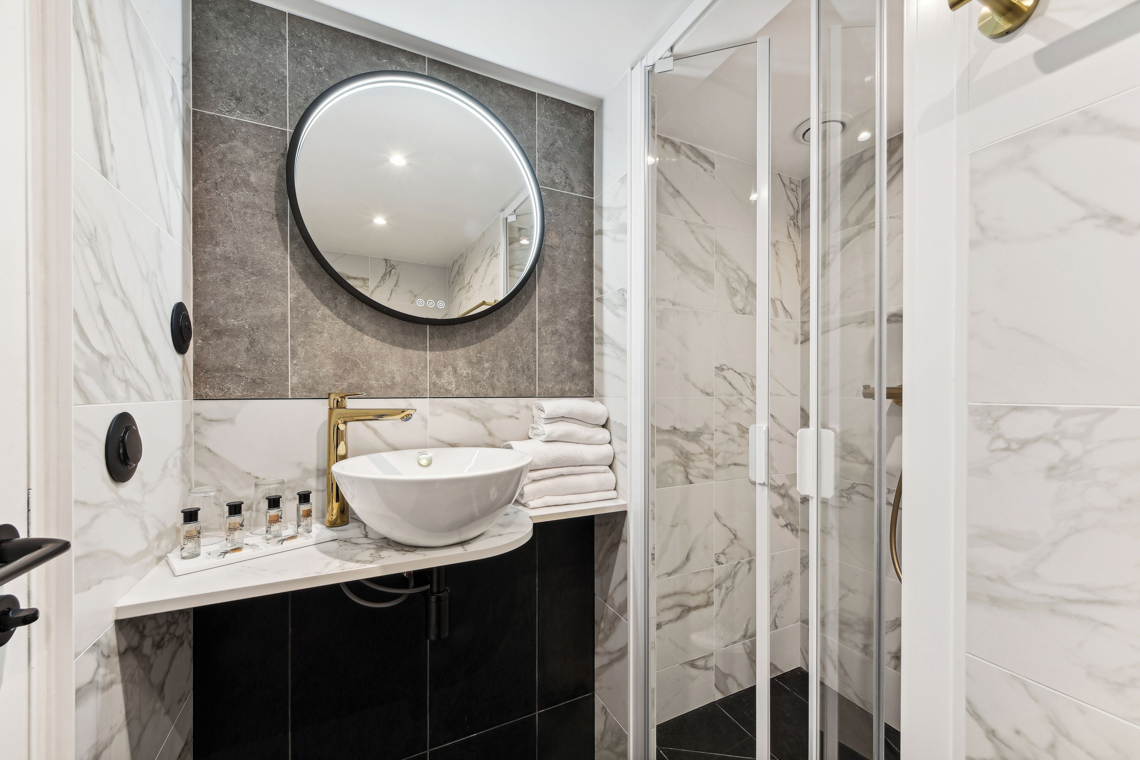 Een moderne badkamer met een ronde spiegel, een witte wastafel en marmeren tegels.