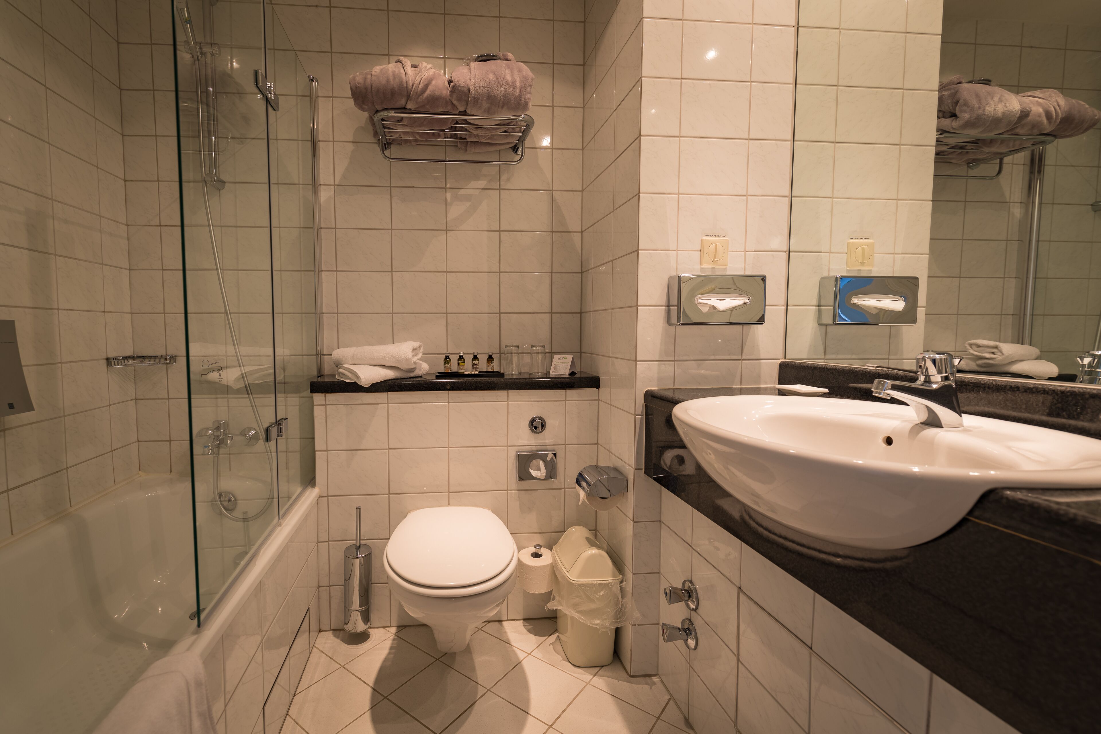 Un baño moderno con ducha de vidrio, inodoro blanco, lavamanos y espejo.