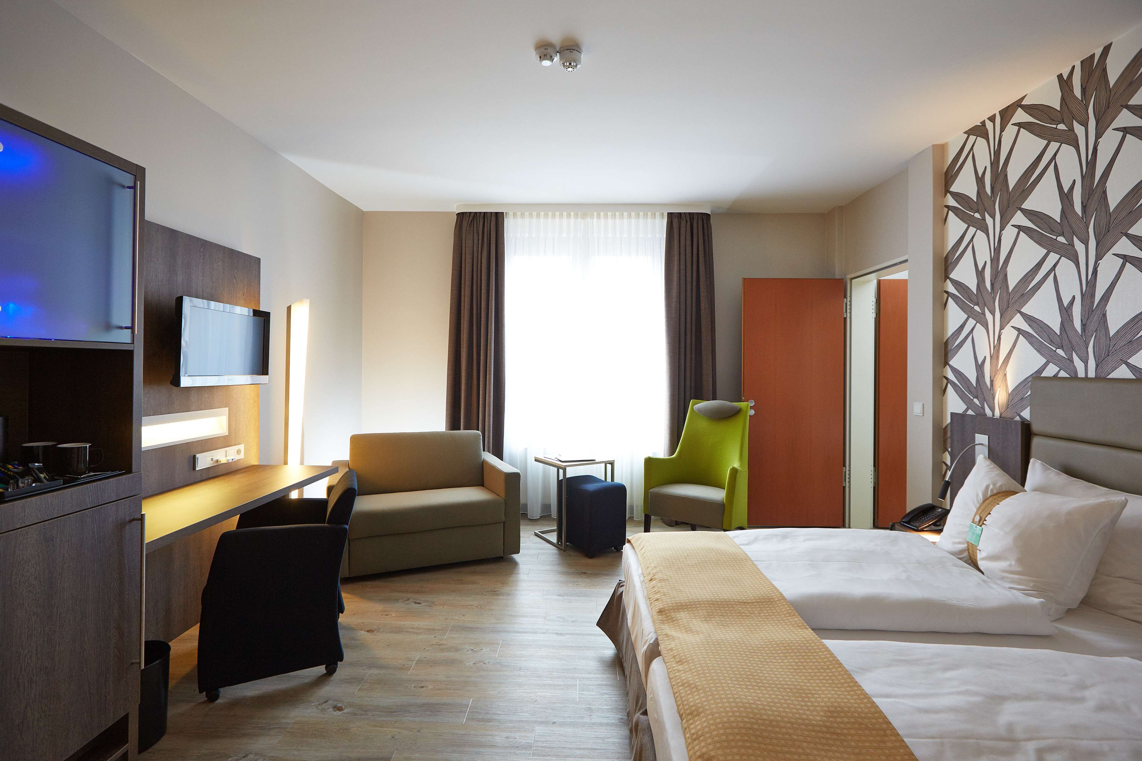 A hotel room with a bed, a desk, a television, a chair, and a sofa.